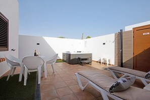 Un patio al aire libre con sillones blancos, una mesa con sillas y un jacuzzi.