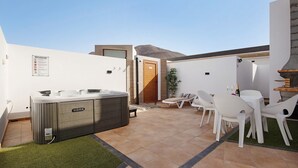 A modern outdoor patio with a hot tub, white lounge chairs, and a small table.