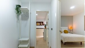 A narrow hallway leading to a bedroom with a bed, a nightstand, and a bedside lamp.