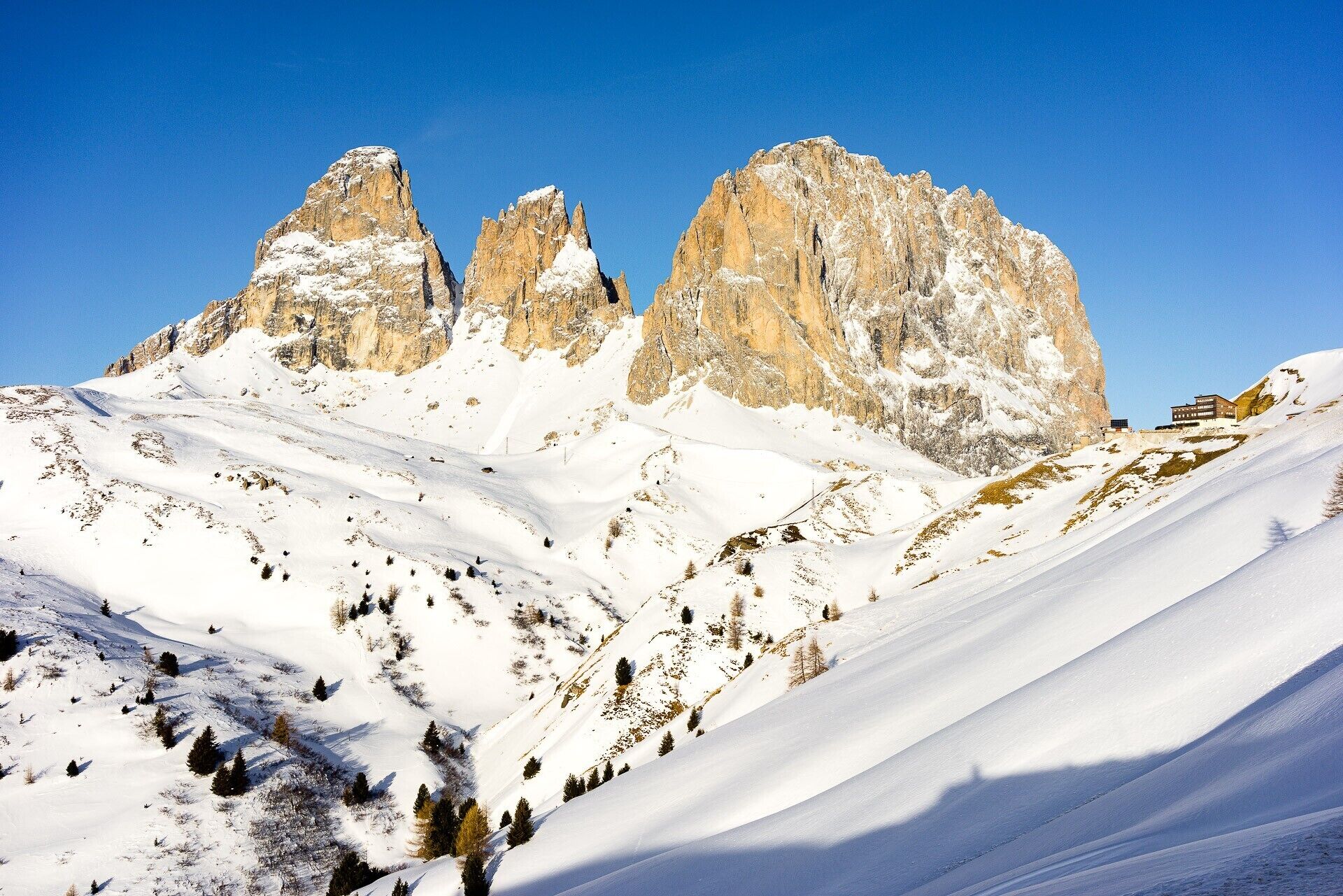 Eine verschneite Berglandschaft mit felsigen Gipfeln und vereinzelten Bäumen.