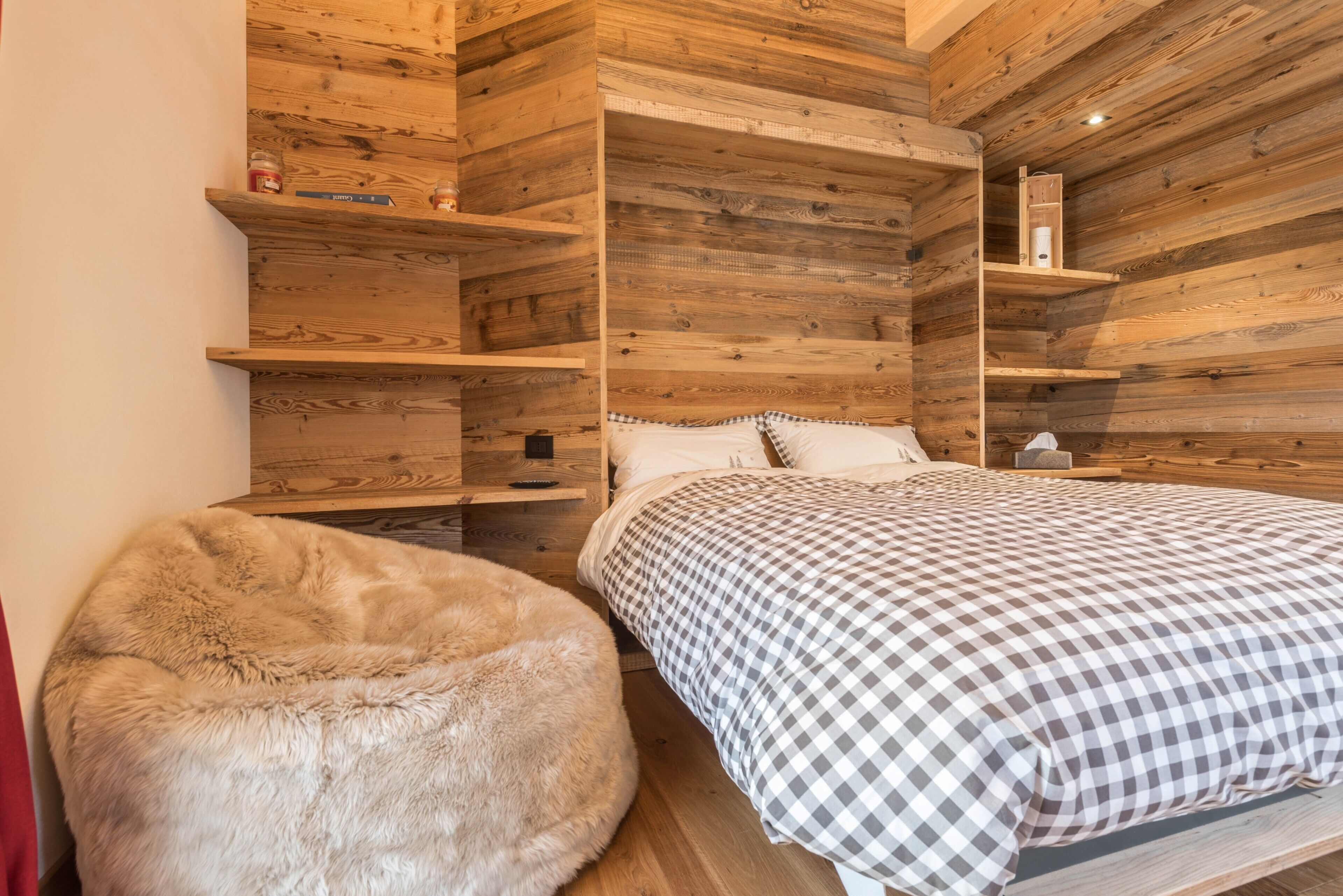 A wooden cabin-style bedroom with a bed, a fluffy ottoman, and built-in shelves.