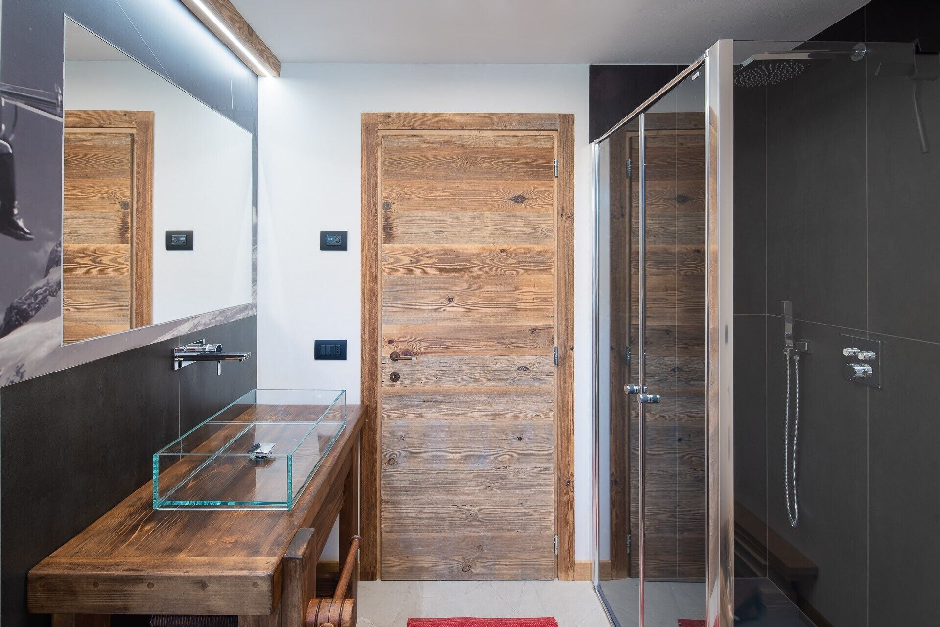 Een moderne badkamer met een houten wand, een glazen wastafel en een inloopdouche.