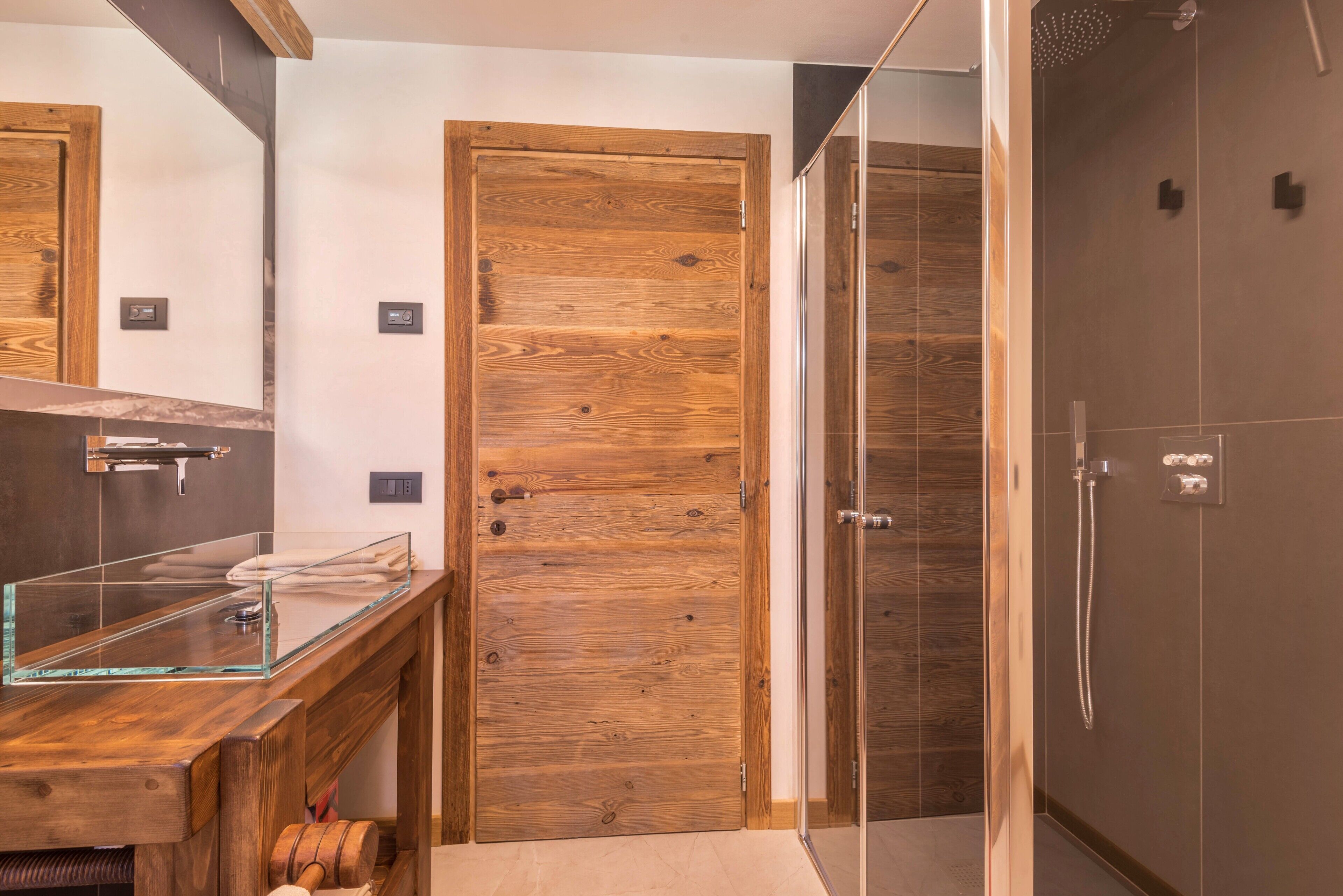 A bathroom with a wooden door, a glass shower enclosure, and a wooden vanity with a glass sink.