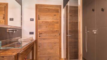 A bathroom with a wooden door, a glass shower enclosure, and a wooden vanity with a glass sink.