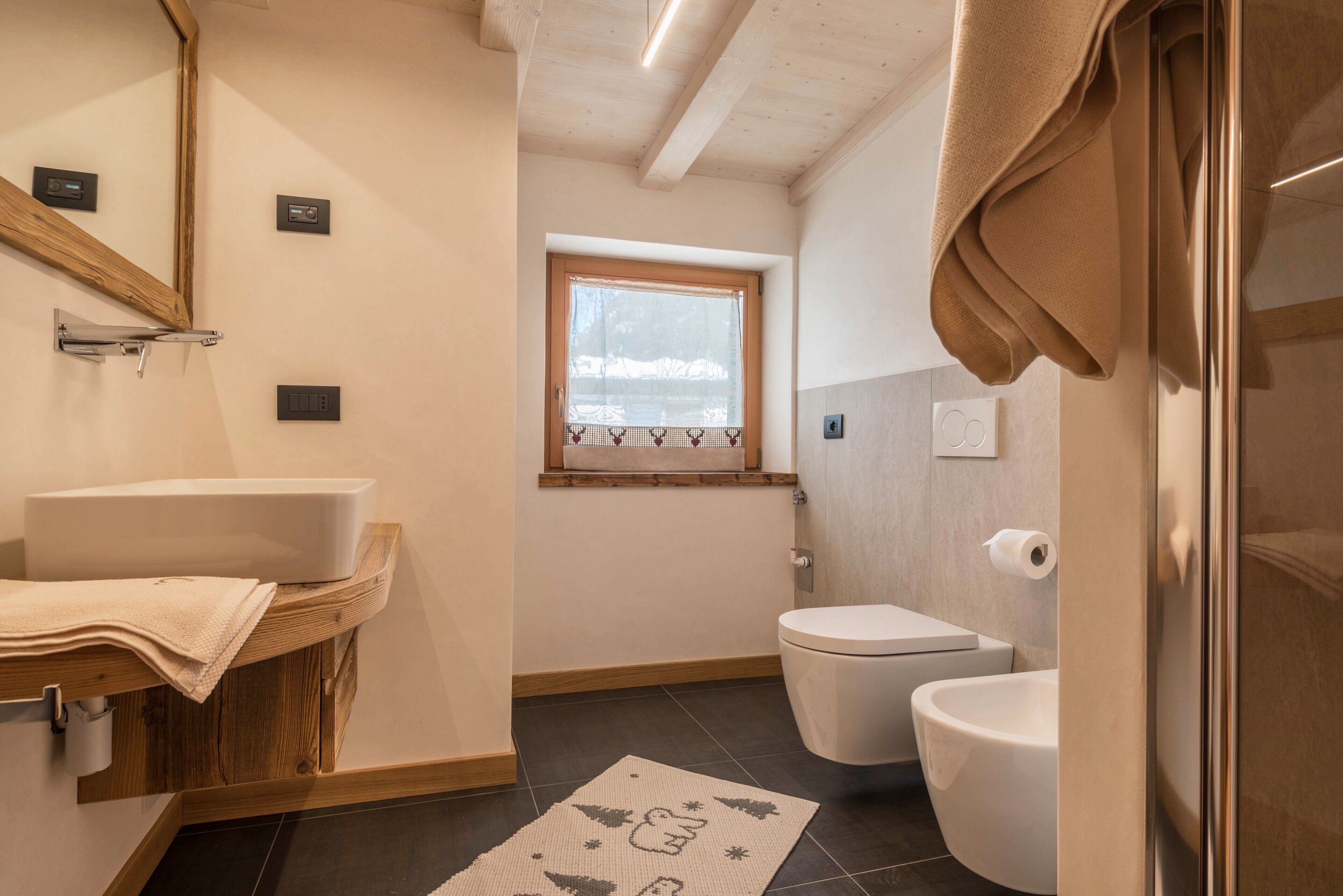 Une salle de bain avec un meuble-lavabo en bois, des toilettes, une fenêtre et une serviette accrochée à la porte.