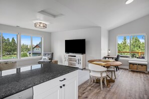 A modern kitchen with a large island, a dining area with a round table, and a flat-screen TV mounted on the wall. - Dara 30 Day - Modern Irish Guest House on Private Estate, Mountain Views (Bend)