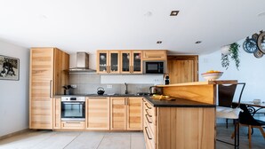 Une cuisine moderne avec des meubles en bois, un four encastré, un four à micro-ondes et un coin repas comprenant une chaise et une table.