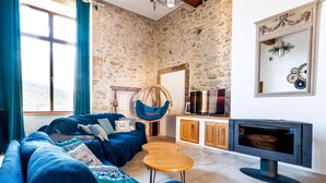 Un salon avec un mur en pierre, un canapé bleu, un fauteuil suspendu, une table basse en bois et une cheminée.