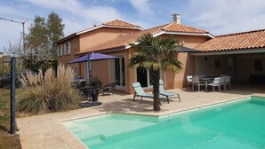 Ein zweistöckiges Haus mit Schwimmbad, Sitzgelegenheiten im Freien und einer Terrasse.