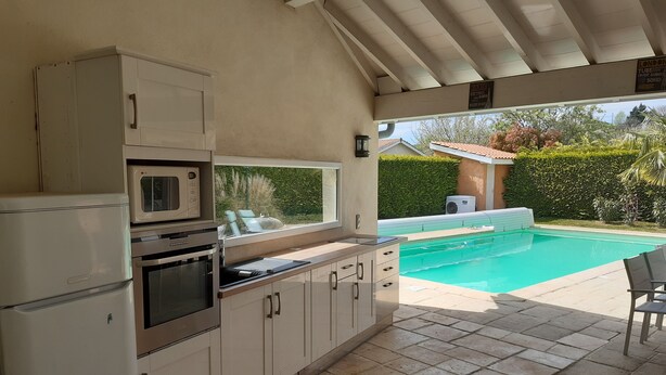 Eine Küche mit Einbauofen, Mikrowelle und Kühlschrank. Ein Fenster bietet Blick auf einen Swimmingpool und einen Garten.