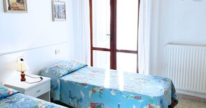 Un dormitorio con dos camas, una mesita de noche, una lámpara y una ventana con cortinas.