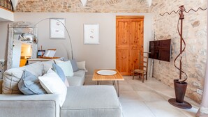Una sala de estar acogedora con una pared de piedra, una puerta de madera y un televisor. Hay un sofá, una mesa y una lámpara de pie.