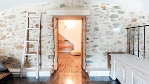 Una habitación con paredes de piedra, una escalera de madera, un banco y un armario blanco.