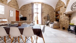 Un comedor amplio con una mesa preparada para cuatro personas, un sofá y una televisión en una habitación de paredes de piedra y techos abovedados.