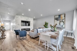 Un espace repas moderne avec une cheminée en marbre, des chaises de salle à manger blanches et un grand tableau accroché au mur.