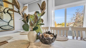 Ein Essbereich mit Tisch, gedeckt für zwei Personen, inklusive einer Vase mit grünen Blättern, einer Schale mit Steinen und gewebten Tischsets.