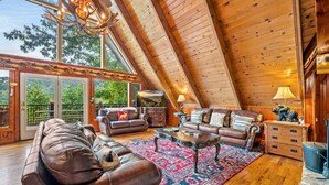 A spacious loft-style living room with a high ceiling, large windows, and a view of the outdoors.