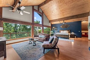 A spacious living area with a high ceiling, large windows, a wooden floor, a sofa, a chair, and a bed. - Unwind at Ozark Outdoor! Nestled in Nature-Pvt Firepit & Hot Tub-Near Big Cedar Cozy (Ridgedale)