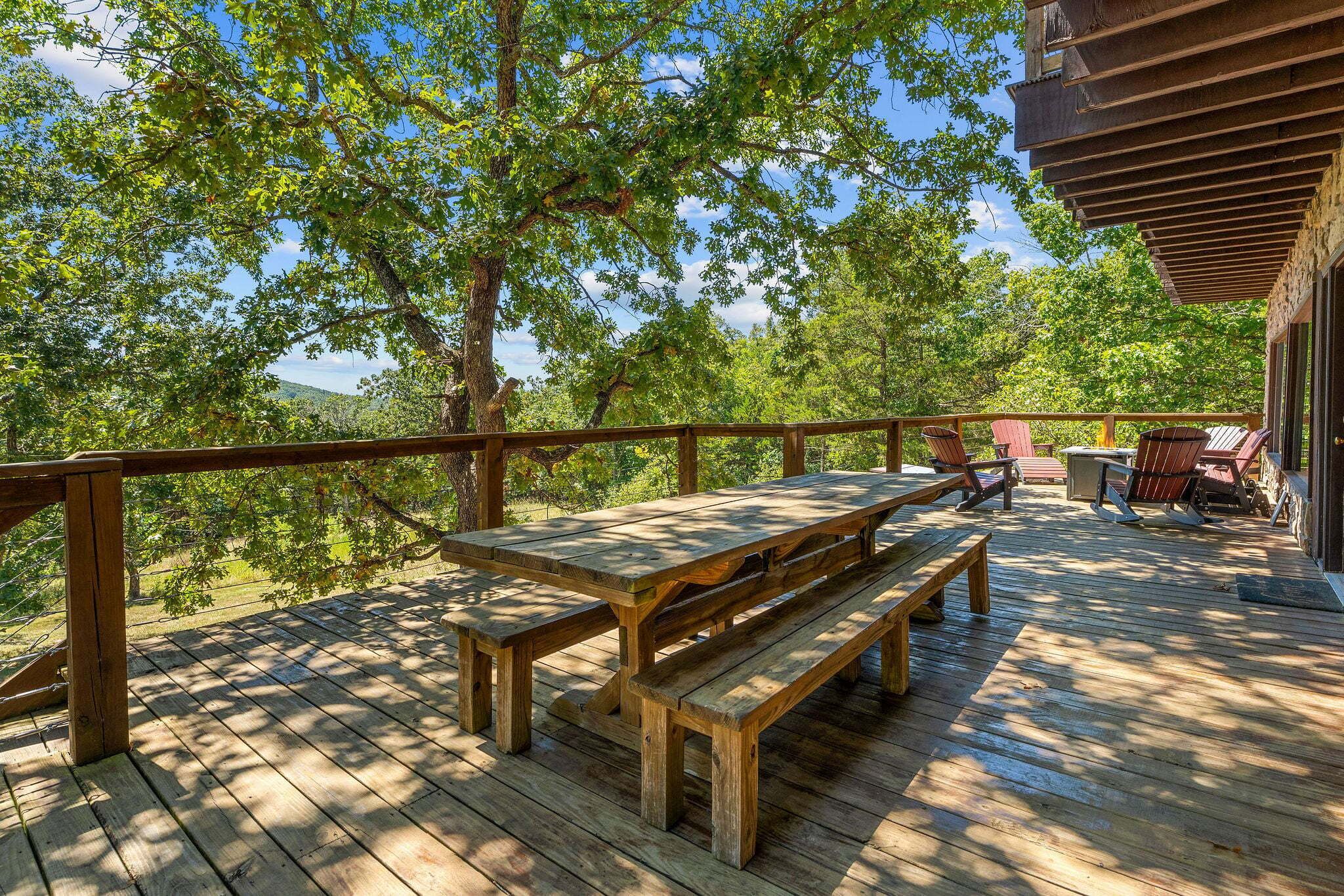 Eine Holzterrasse mit Picknicktischen und Adirondack-Stühlen, umgeben von Bäumen.