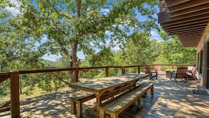 Een houten terras met picknicktafels en Adirondack-stoelen, omringd door bomen.
