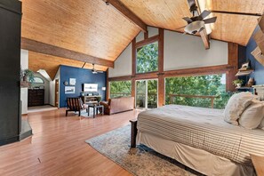 A spacious bedroom with a large bed, a desk, and a chair, and a view of the outdoors through large windows. - Unwind at Ozark Outdoor! Nestled in Nature-Pvt Firepit & Hot Tub-Near Big Cedar Cozy (Ridgedale)