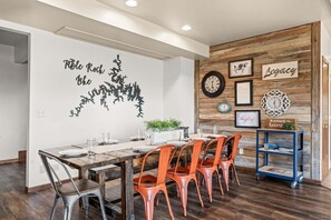 A dining area with a wooden table and chairs, a wall with framed pictures and a clock, and a blue cart with items on it. - Unwind at Ozark Outdoor! Nestled in Nature-Pvt Firepit & Hot Tub-Near Big Cedar Cozy (Ridgedale)
