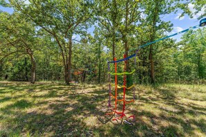 A natural outdoor area with trees and a colorful rope swing structure.