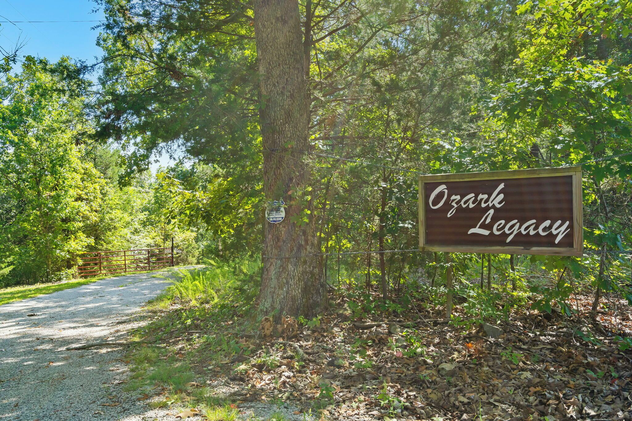 Ein Schild mit der Aufschrift 'Ozark Legacy' in einer bewaldeten Gegend mit einem Schotterweg.