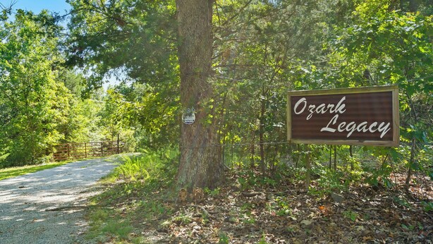 Een bord met de tekst 'Ozark Legacy' in een bebost gebied met een grindpad.