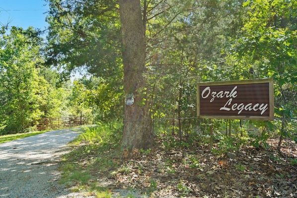 A sign reading "Ozark Legacy" in a wooded area with a gravel path. - Unwind at Ozark Outdoor! Nestled in Nature-Pvt Firepit & Hot Tub-Near Big Cedar Cozy (Ridgedale)