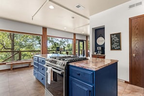 A kitchen with a central island, a coffee bar sign, and a view of trees through large windows.