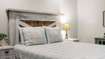Uma cama com cabeceira acolchoada, duas almofadas, uma luminária de cabeceira e uma mesa de cabeceira com gaveta.