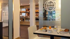 A breakfast area with a table set for two, including a bowl of cereal, a croissant, a muffin, a glass of orange juice, and a plate with a sandwich. - B&B Hotel Frankfurt-hahn Airport (Lautzenhausen)