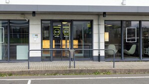 A hotel entrance with glass doors, a metal railing, and a paved sidewalk. - B&B Hotel Frankfurt-hahn Airport (Lautzenhausen)