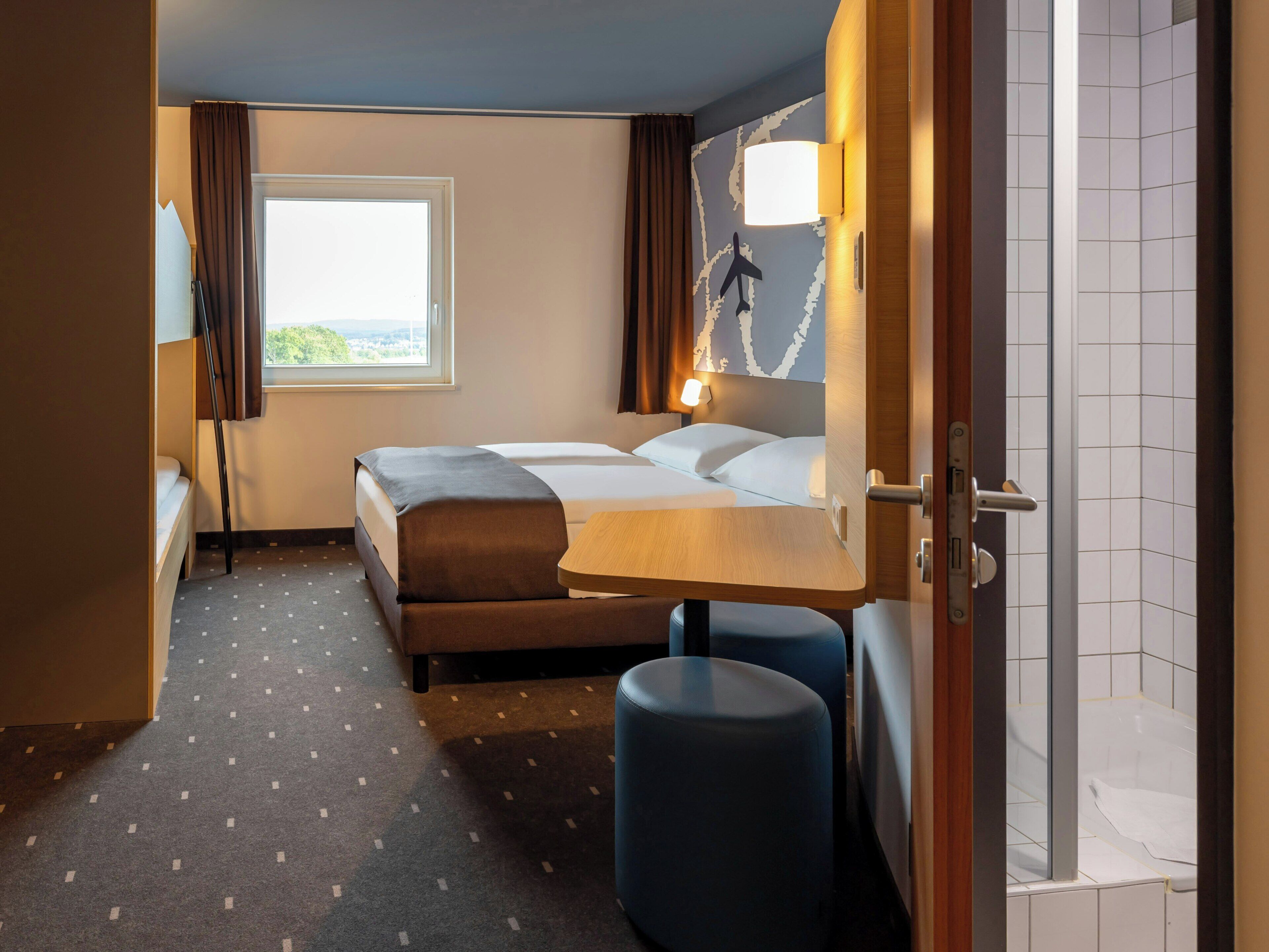 Une chambre d’hôtel avec un lit, un bureau, une chaise et une fenêtre donnant sur un paysage agréable.
