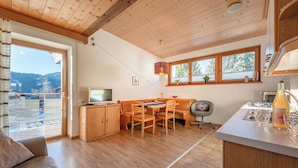 A modern kitchen with wooden cabinets, a dining area with a table and chairs, and a large window with a view of the mountains.