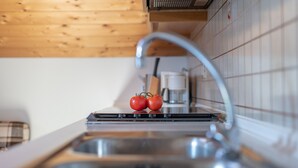 A kitchen with wooden ceiling, a stainless steel sink, and two tomatoes on the counter.