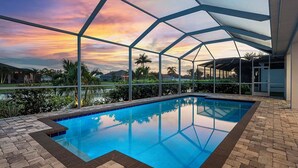 Ein Innenpool mit freiem Blick auf den Sonnenuntergang durch eine Glasfassade, umgeben von einer Ziegelterrasse und einem überdachten Sitzbereich.