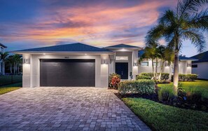 Ein modernes Haus mit Garage, befestigter Auffahrt und gepflegter Bepflanzung, darunter eine Palme und Sträucher.