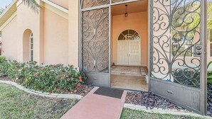 A building entrance with a decorative metal gate, a white door, and a pathway leading to the entrance. - Summer Breeze - Gulf Access Location - Pool & Hot (Cape Coral)