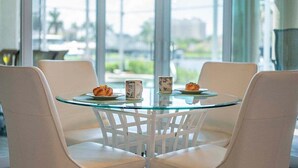 Una mesa con cubierta de vidrio, sillas blancas, dos platos con pasteles y dos tazas con diseños florales.