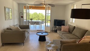 Amplia sala de estar con dos sofás, una mesa de centro y un televisor. Se puede ver un comedor con sillas y una mesa a través de una puerta abierta.