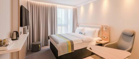 A hotel room with a bed, a desk, a chair, a TV, and a window with curtains.