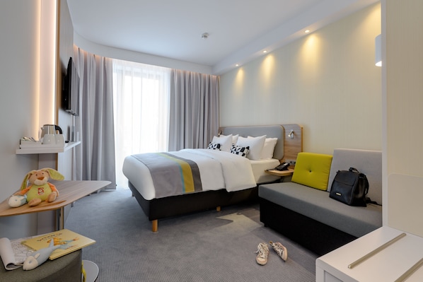 A modern hotel room with a bed, a sofa, a desk, and a TV.