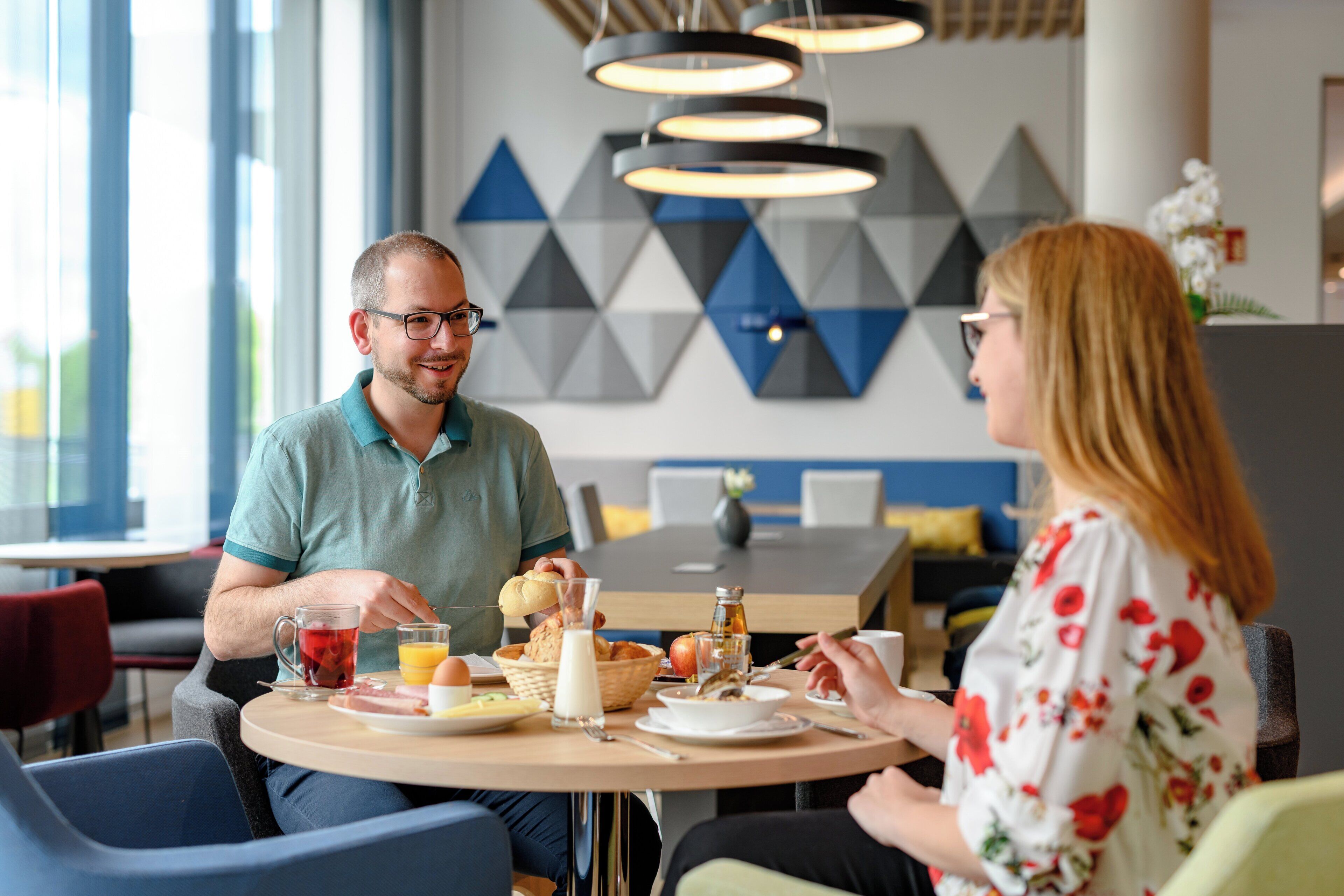 A dining area with a round table, chairs, and a variety of breakfast items including bread, fruit, and beverages.