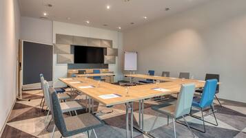 A conference room with a large table, chairs, a whiteboard, and a flat-screen TV.