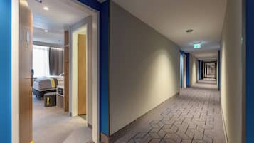 Ein Hotelgang mit einem geometrisch gemusterten Boden, einem Bett und einem Schreibtisch mit Stuhl.