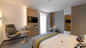 Una habitación de hotel moderna con una cama grande, un escritorio, una silla, un televisor de pantalla plana y una mesita.