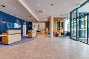 A modern reception area with a wooden reception desk, seating area with colorful chairs, and a glass wall offering a view outside. - Holiday Inn Express Fulda by IHG (Fulda)