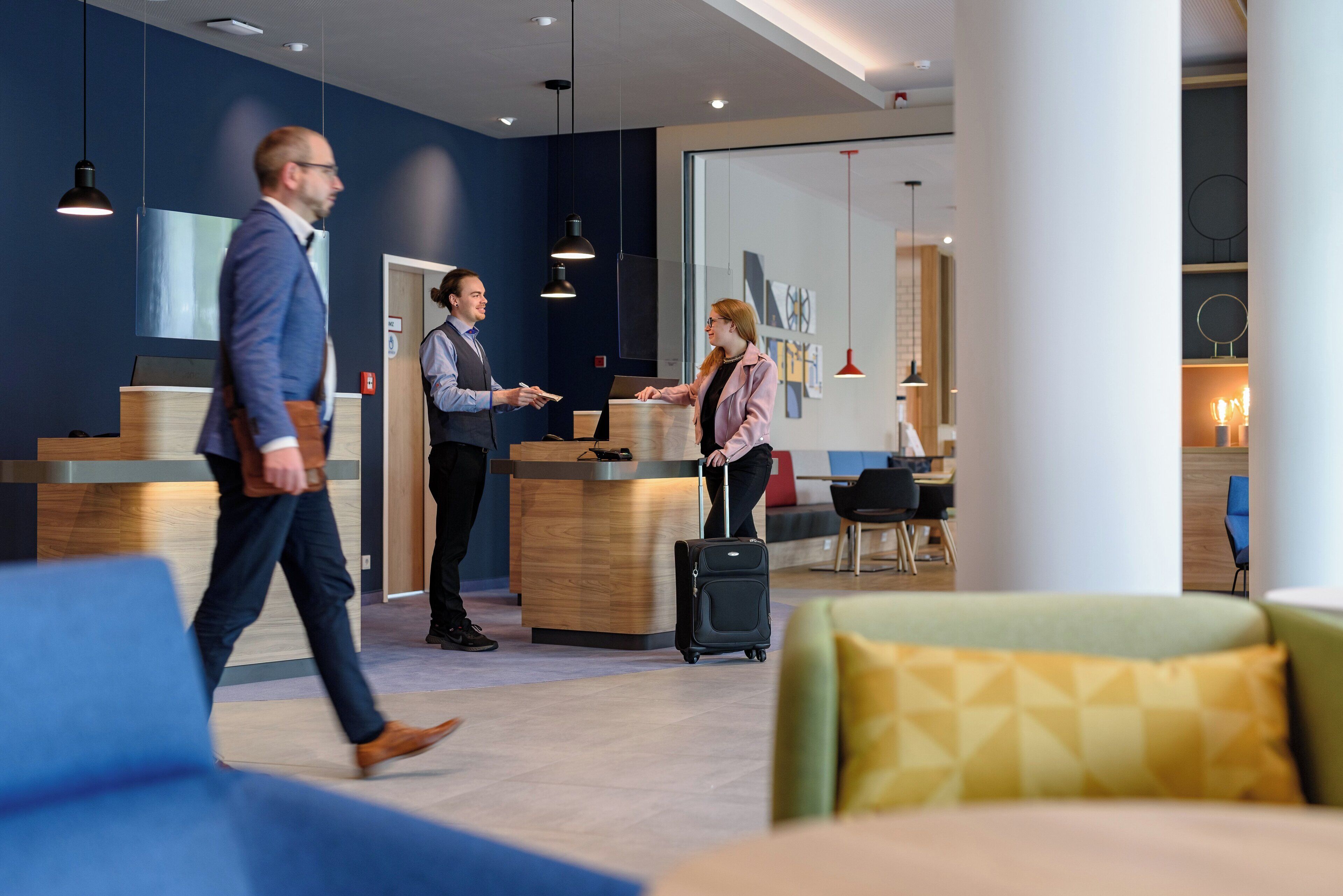 A hotel lobby with a reception desk, seating areas, and a large window.